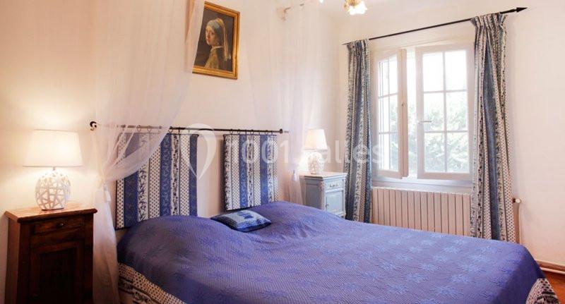 GITE MANGUIN Chambre lumineuse avec lit double bleu, rideaux assortis, deux lampes de chevet et un tableau au mur.