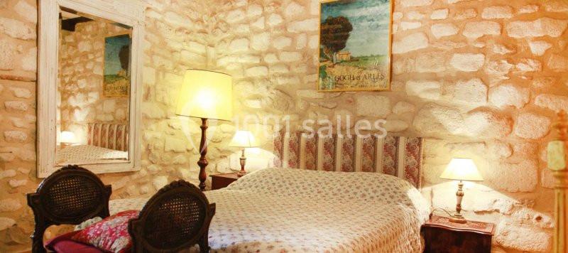 GITE VAN GOGH Chambre rustique avec murs en pierre, lit double, lampes de chevet et miroir encadré.