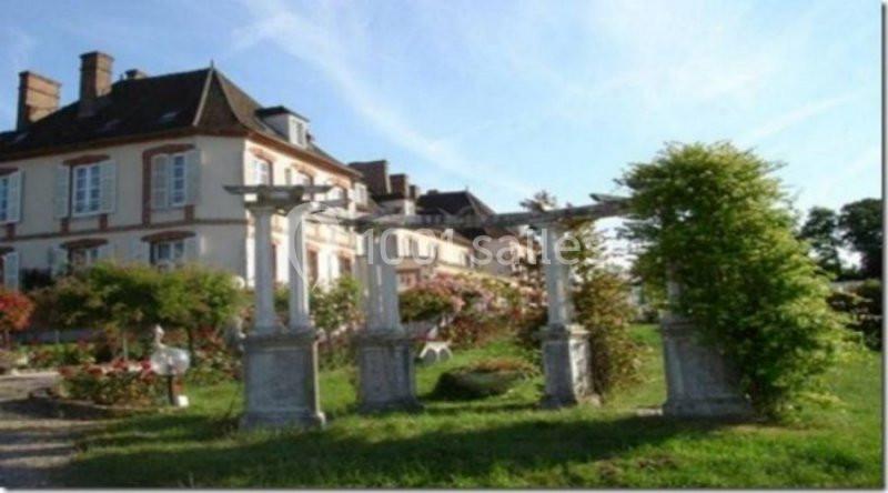 Façade d'un bâtiment ancien entouré d'un jardin fleuri avec des colonnes décoratives en pierre au premier plan.