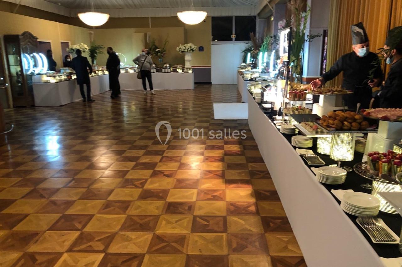 Salle de réception avec buffet varié, tables dressées et quelques personnes servant ou se déplaçant.