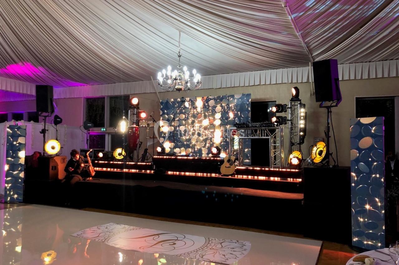 Scène décorée avec éclairages colorés, instruments de musique et fond lumineux dans une salle de réception sous chapiteau.