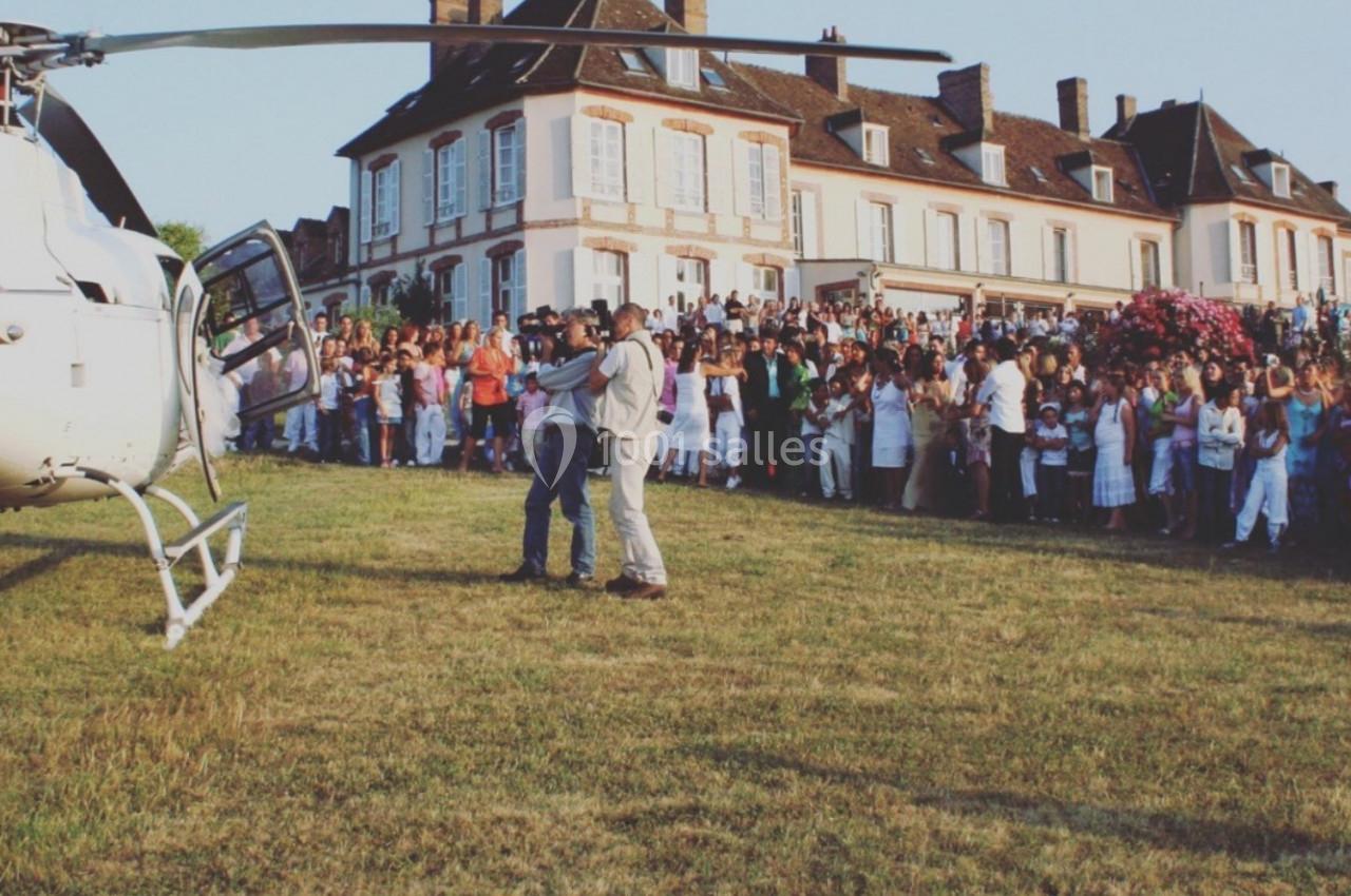 Un hélicoptère posé sur une pelouse devant une grande maison, avec une foule rassemblée en arrière-plan.