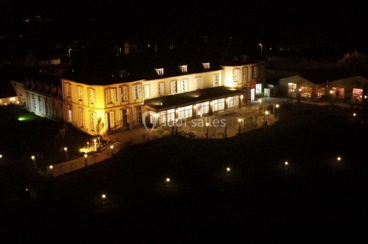 Vue nocturne d'un grand bâtiment éclairé, entouré de lumières et de jardins.