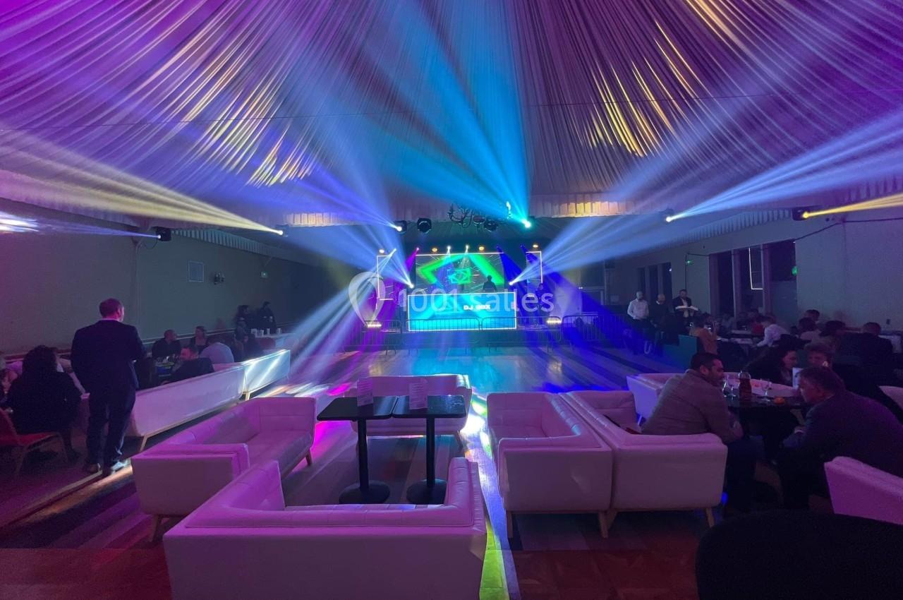 Salle de réception avec éclairage coloré, piste de danse centrale et canapés blancs disposés autour.