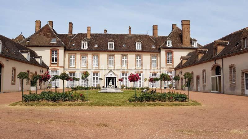 Cour intérieure d’un manoir avec jardin central fleuri, statue au centre et bâtiments en briques et toits en ardoise.