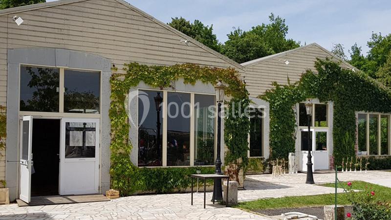 Façade d'un bâtiment en bois avec des murs partiellement recouverts de lierre, entouré d'une terrasse pavée.