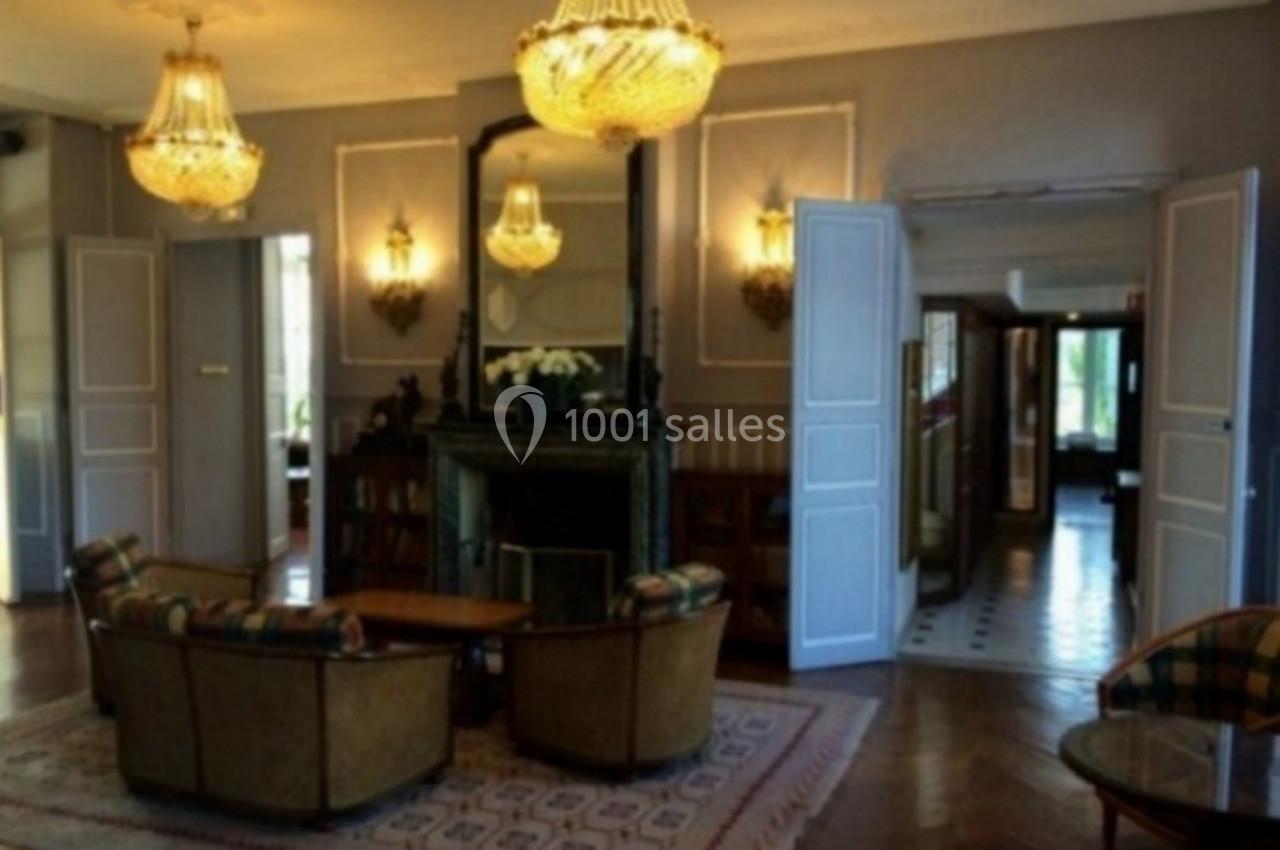 Salon élégant avec cheminée, lustres en cristal, fauteuils autour d'une table basse et parquet en bois.