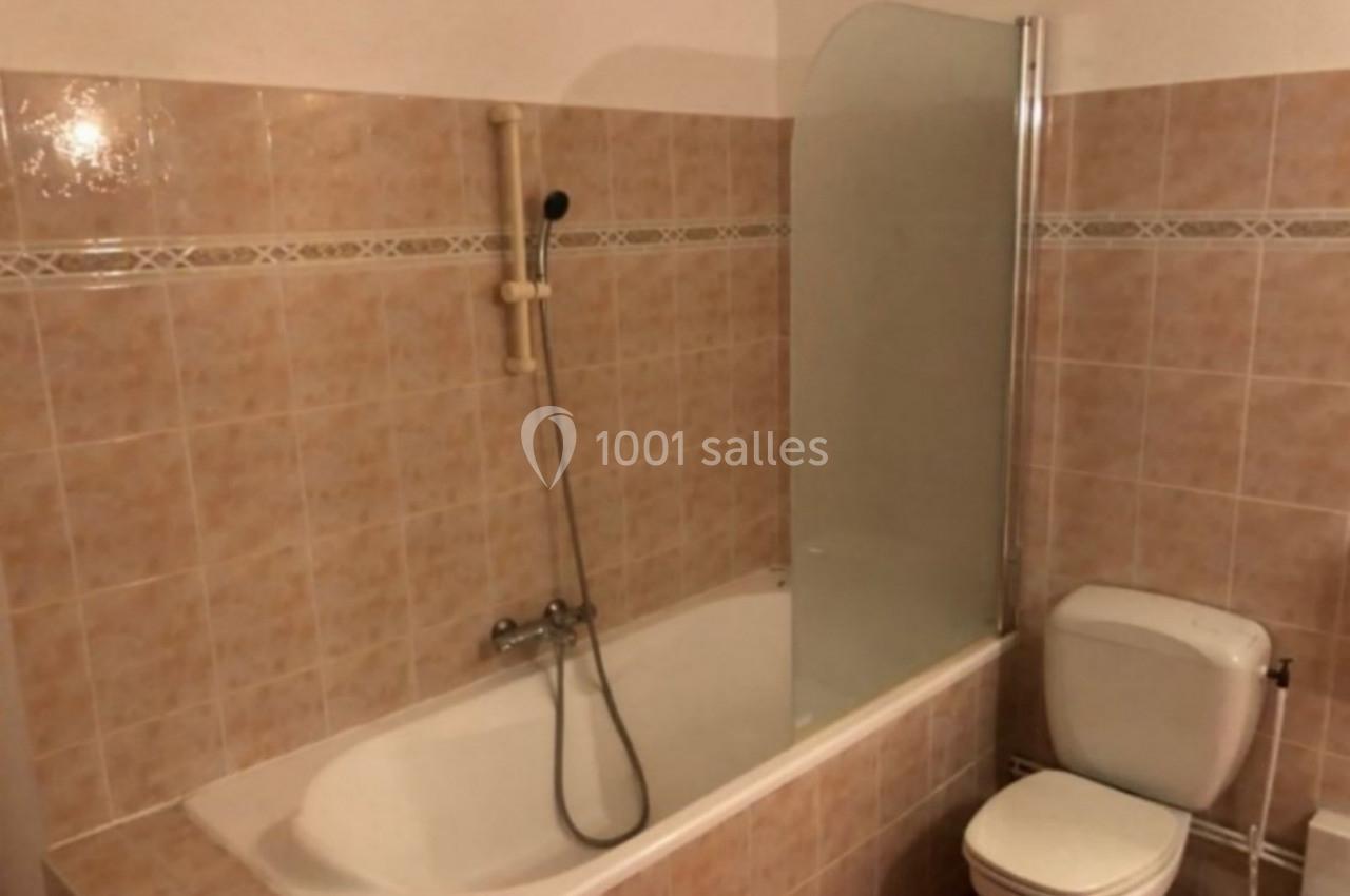 Salle de bain avec baignoire équipée d'une douchette murale, paroi en verre et toilettes adjacentes.