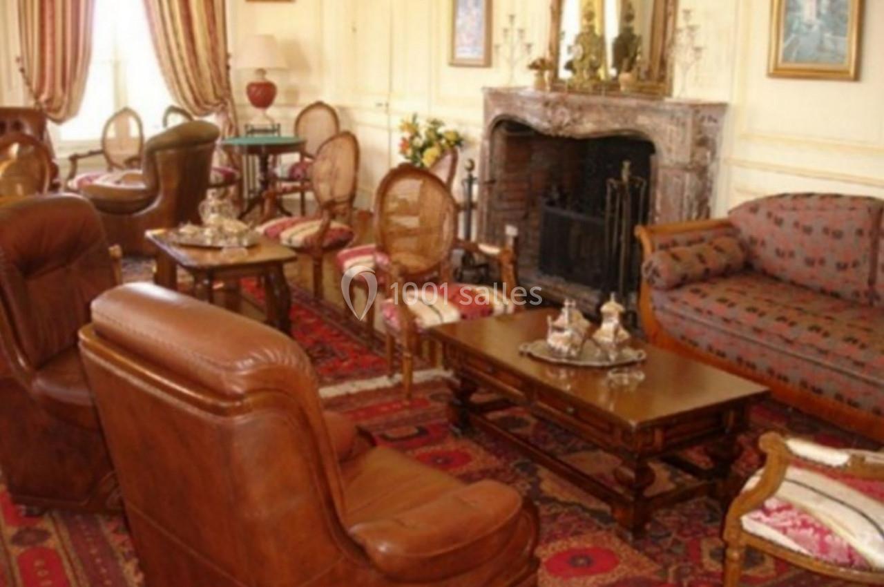 Salon élégant avec mobilier classique, fauteuils en cuir, cheminée en marbre, tapis rouges et décoration raffinée.