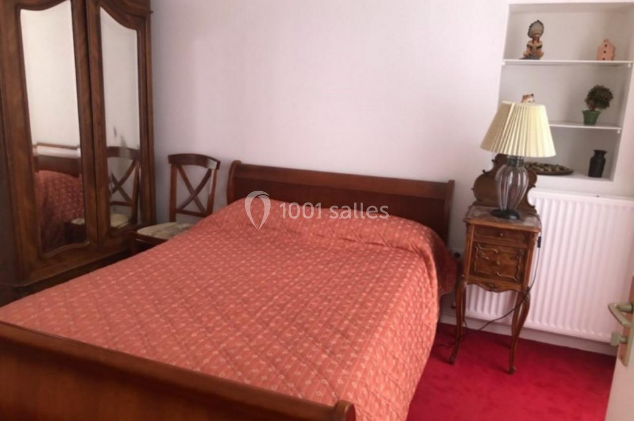 Chambre avec lit double en bois, armoire ancienne, table de chevet avec lampe et étagères décorées.