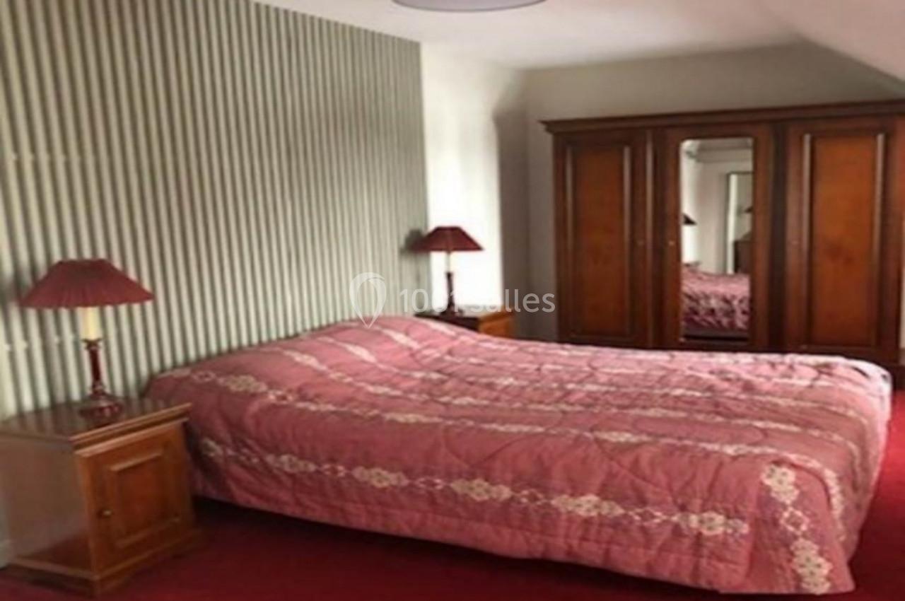 Chambre avec lit double, couvre-lit rose, deux tables de chevet avec lampes et une armoire en bois à miroir.