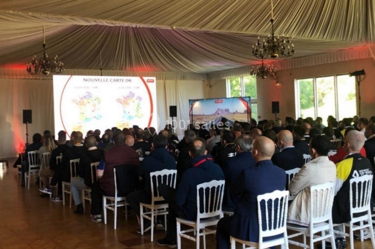 Une conférence dans une salle lumineuse avec un public assis et une présentation projetée sur un écran.