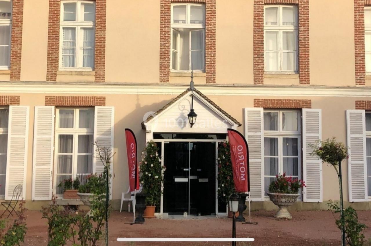 Façade d'un bâtiment avec des volets blancs, une entrée centrale et deux drapeaux rouges près de la porte.