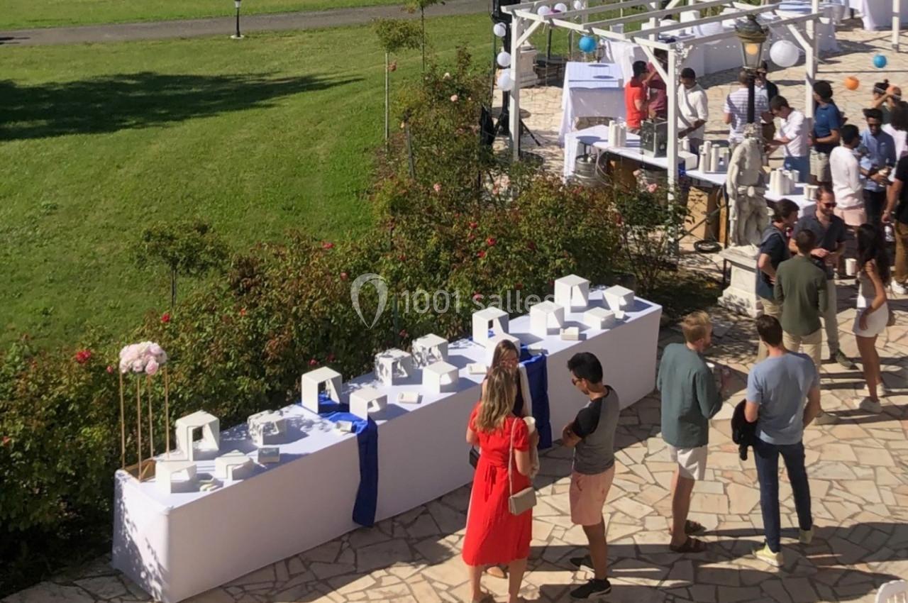 Des invités discutent près d'une table de buffet décorée, dans un jardin lors d'un événement en plein air.