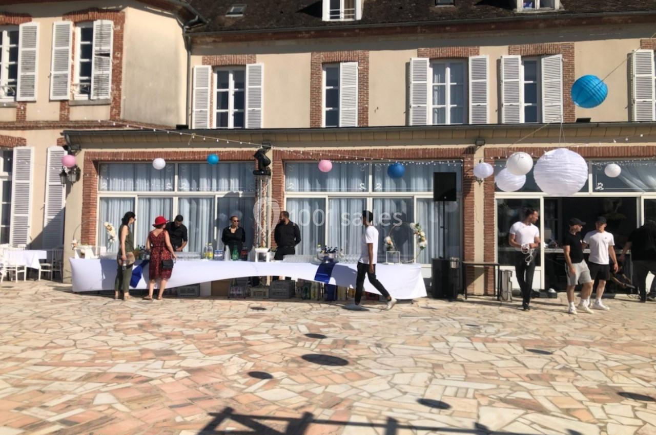 Personnes rassemblées autour d'une table en extérieur devant un bâtiment en briques avec des décorations festives.