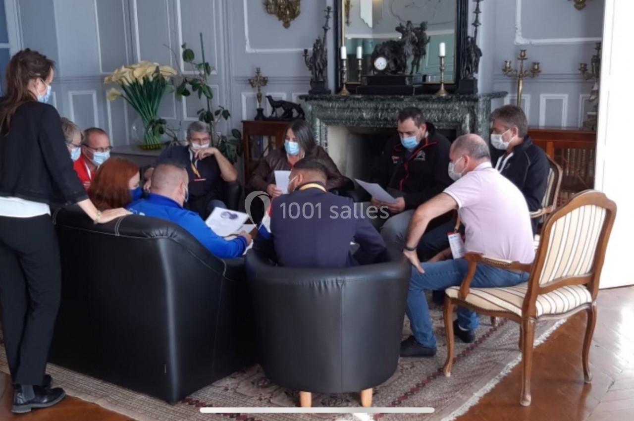 Un groupe de personnes assises en cercle dans un salon, discutant autour de documents, certaines portant un masque.