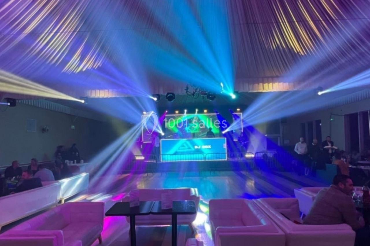 Salle de réception avec éclairage coloré, piste de danse centrale et invités assis autour de tables.