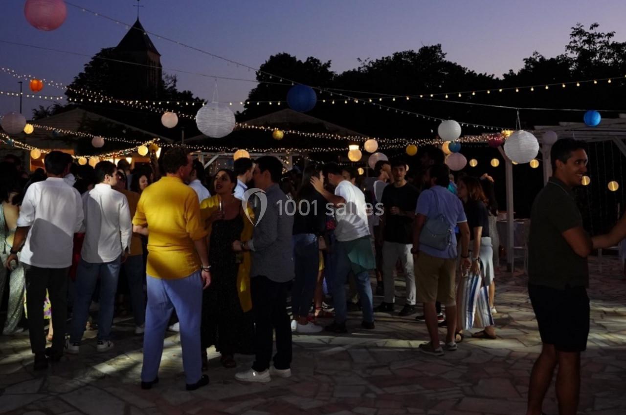Groupe de personnes discutant et célébrant en soirée sous des guirlandes lumineuses et des lanternes suspendues.