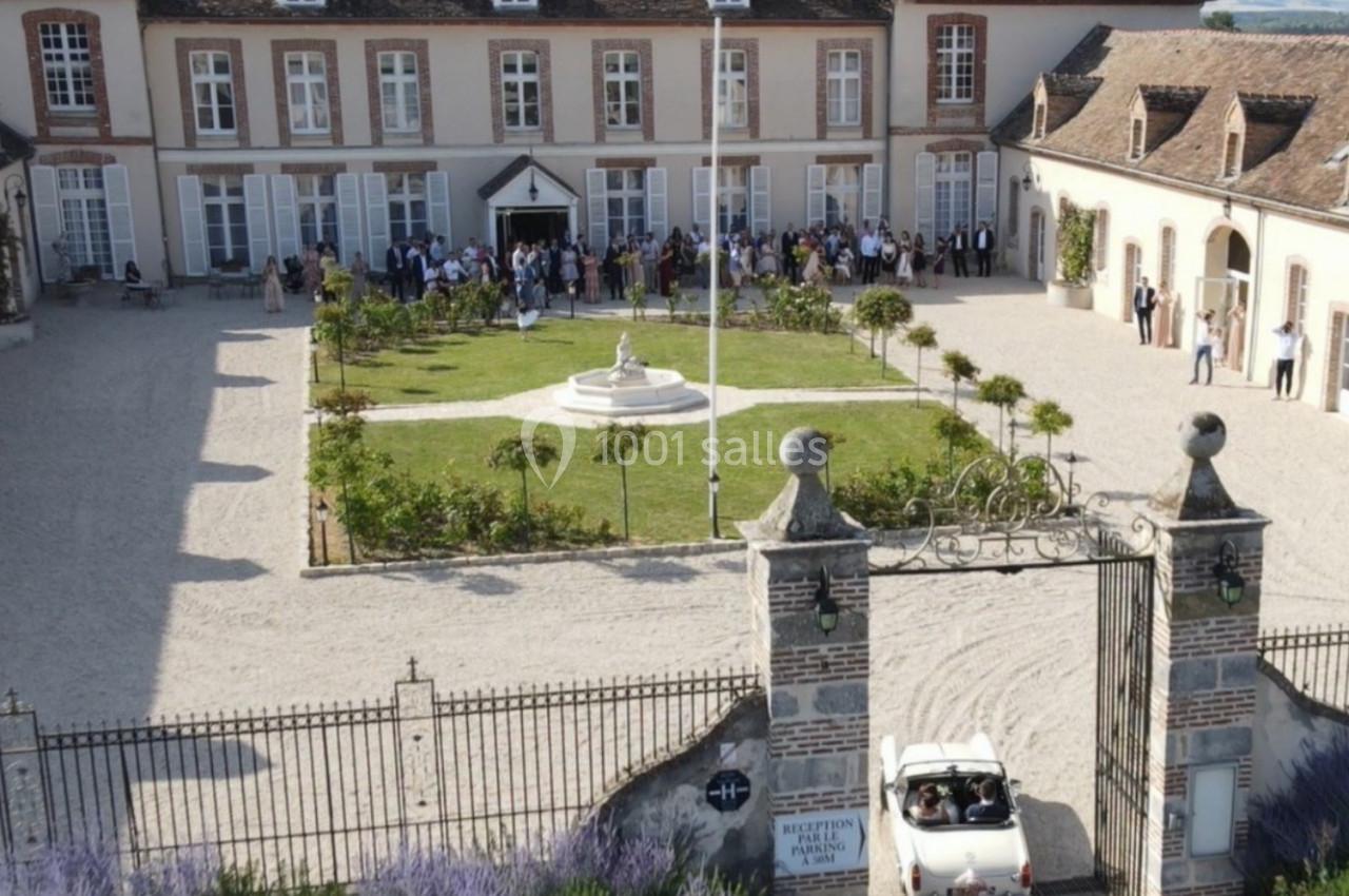 Vue aérienne d'une cour intérieure avec jardin central, entourée de bâtiments anciens, et une voiture blanche entrant par le…