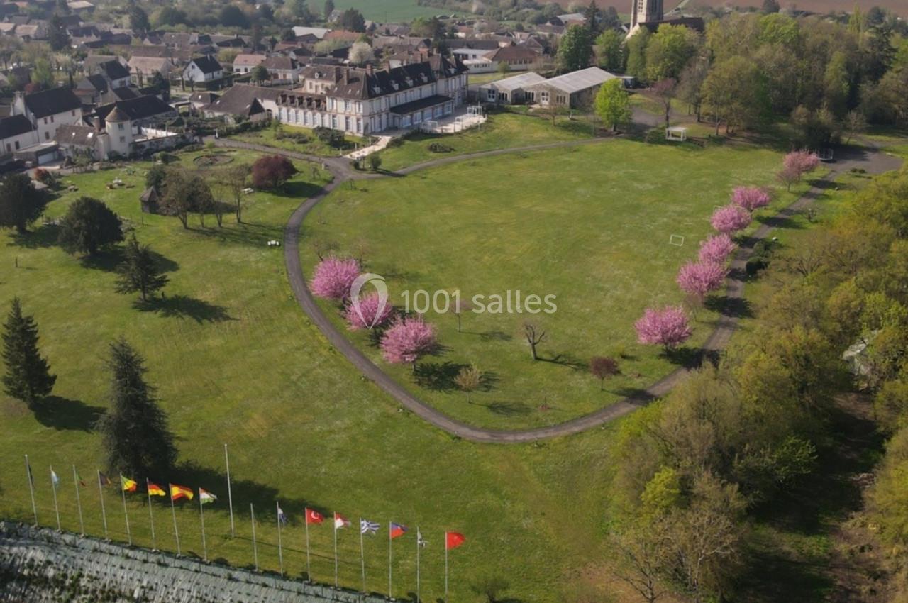 Vue aérienne d'un parc avec pelouse, arbres en fleurs roses, drapeaux alignés et bâtiments résidentiels en arrière-plan.