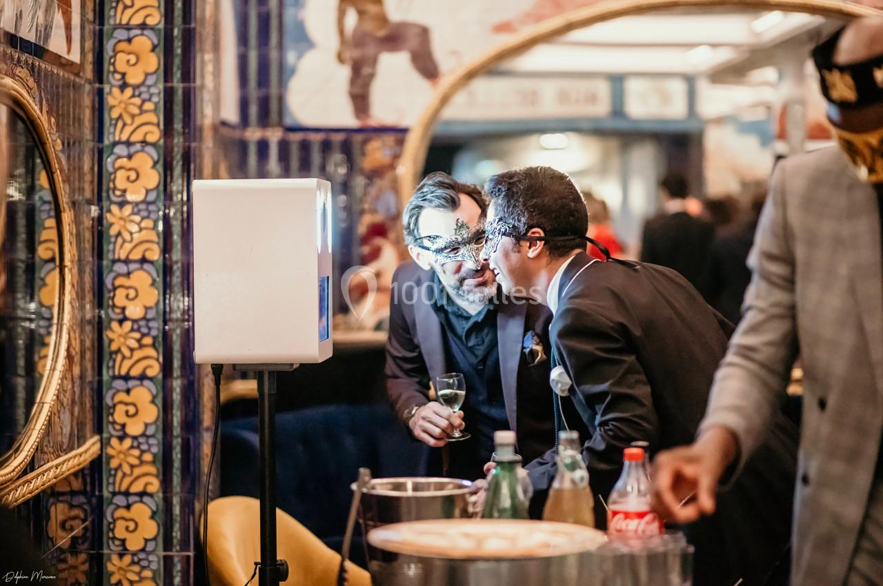 Deux hommes discutent près d'un photobooth dans un espace décoré de carreaux colorés et de miroirs.