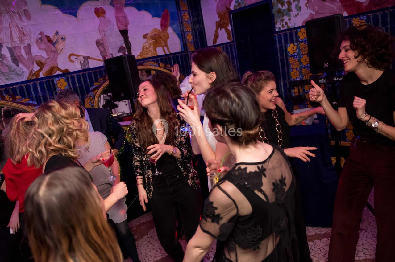 Des personnes dansent et discutent joyeusement lors d'une soirée dans un lieu décoré de fresques colorées.