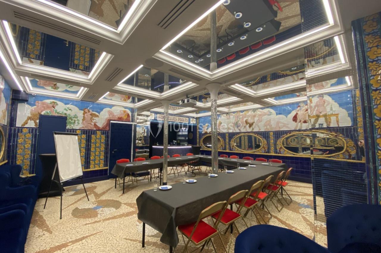 Salle de réunion élégante avec tables en U, chaises rouges, fresques murales colorées et plafond à miroirs.