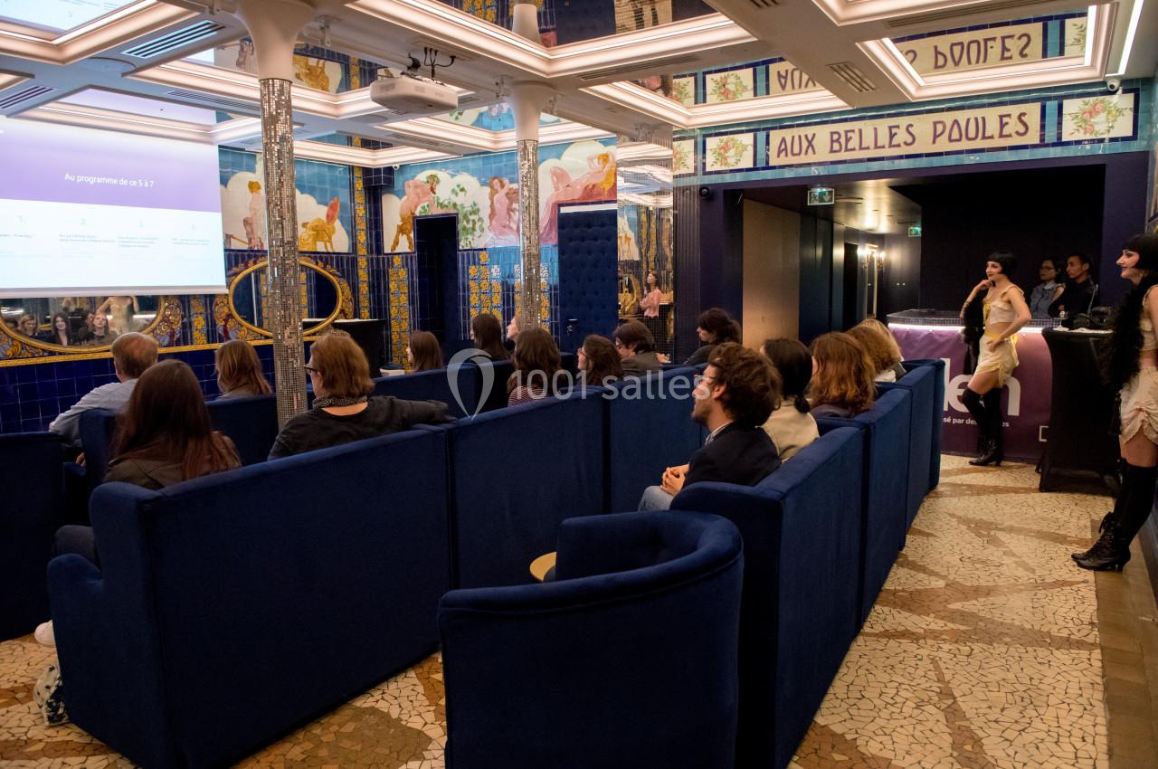 Personnes assises dans une salle colorée avec des fresques murales, regardant une présentation projetée sur un écran.