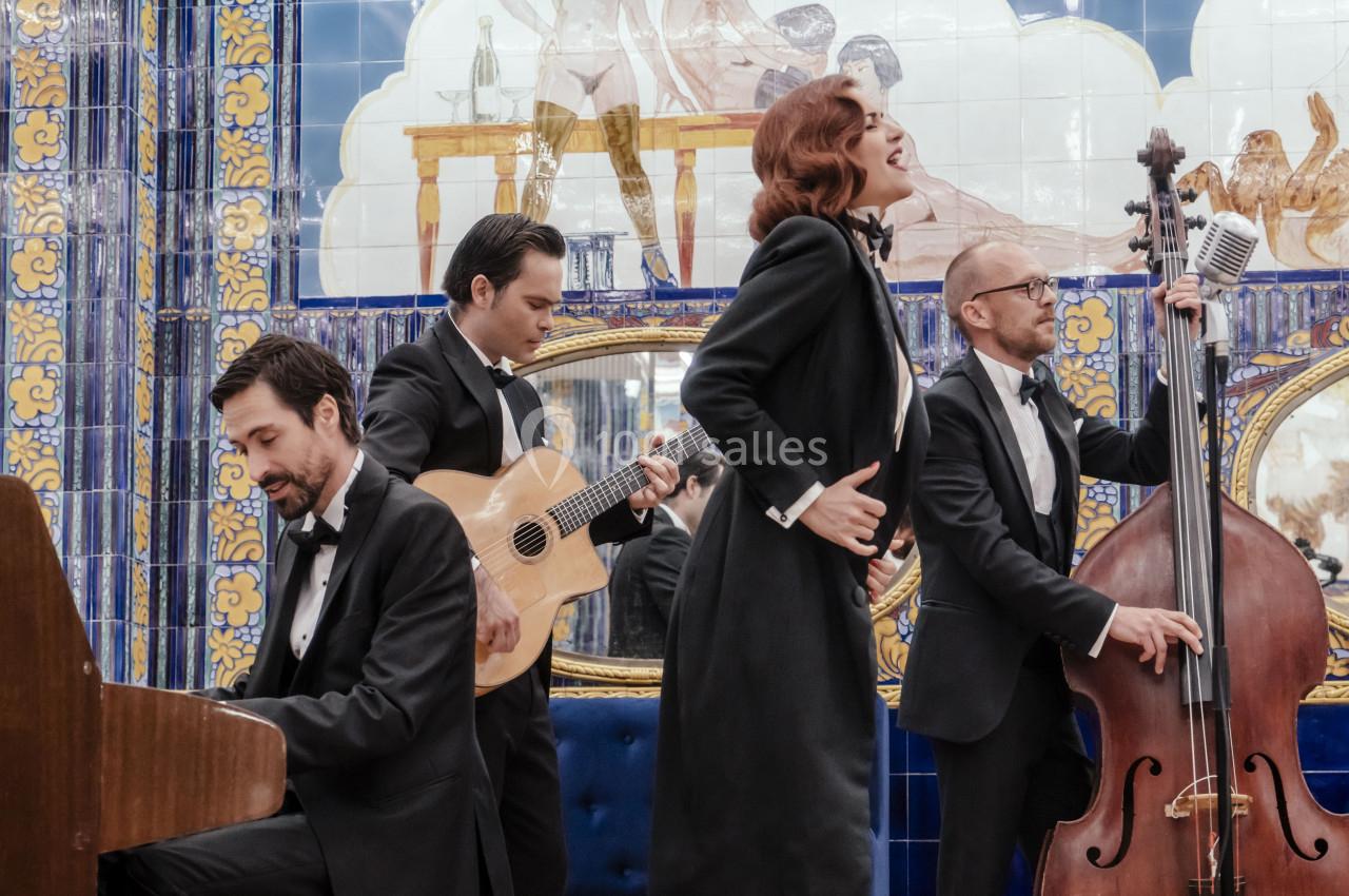 Un groupe en tenue élégante joue de la musique dans une salle décorée de carreaux colorés et de miroirs.