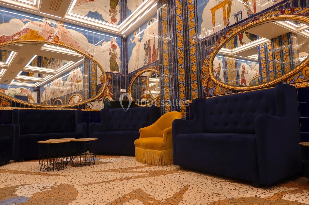 Salon décoré de mosaïques colorées, miroirs ovales, fauteuils bleus et un fauteuil jaune au centre.