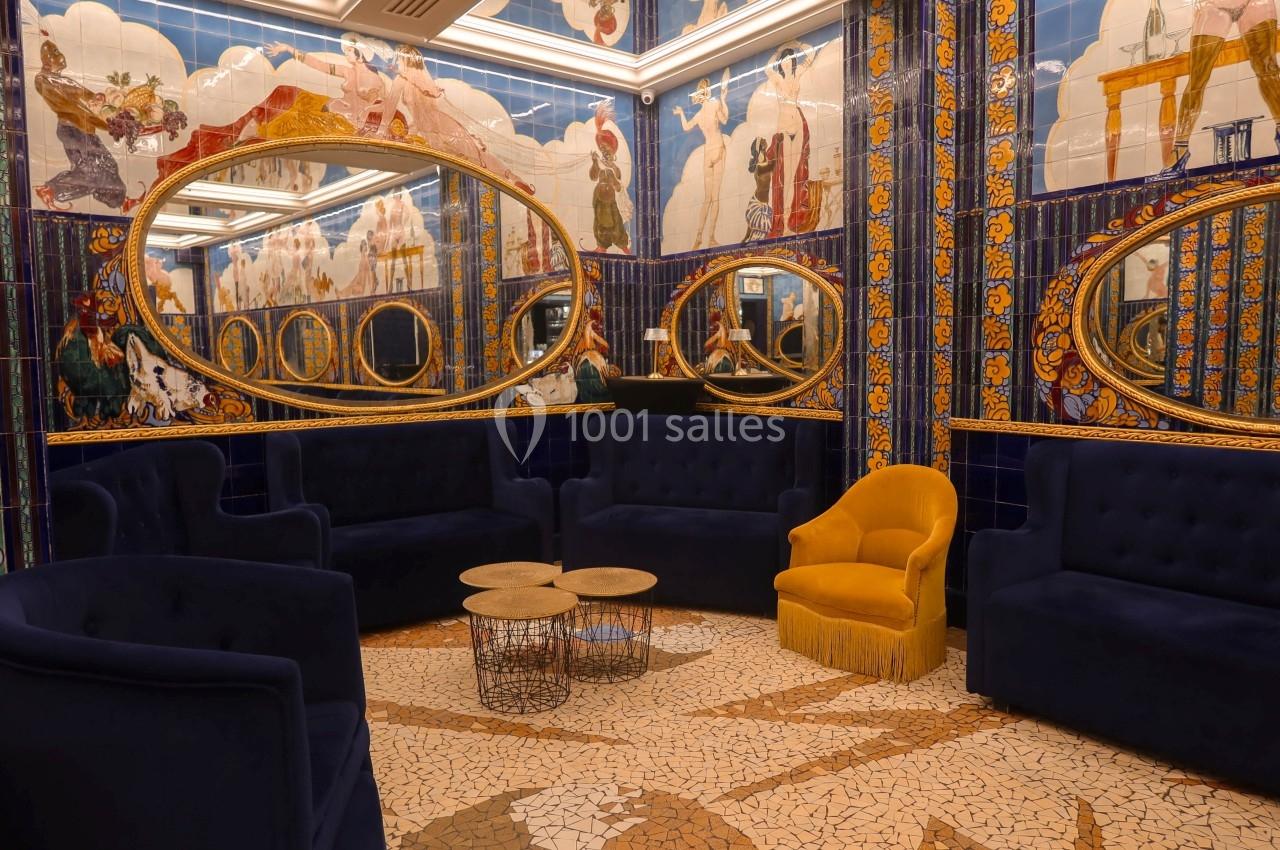 Salon décoré de mosaïques colorées, miroirs ovales dorés, fauteuils bleus et jaunes, et tables basses en métal.