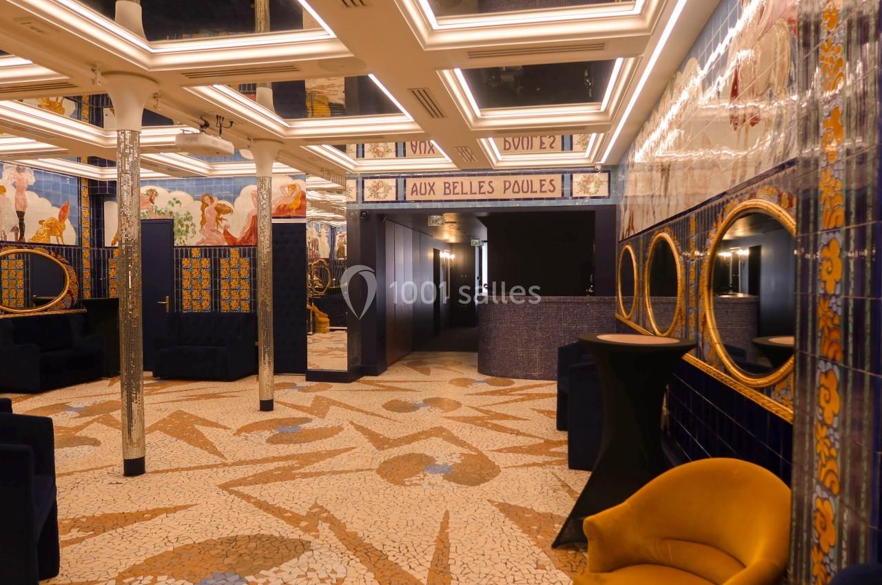 Salle décorée de mosaïques au sol, murs ornés de fresques et miroirs, avec fauteuils et éclairage lumineux.