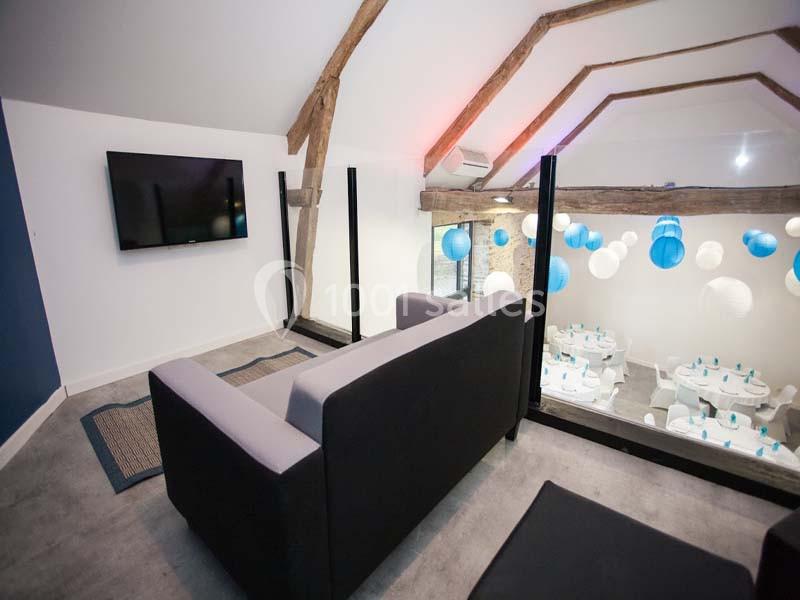 Vue d'une mezzanine avec canapé, télévision murale et aperçu d'une salle décorée de lanternes bleues et blanches.