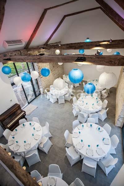 Salle de réception avec tables rondes dressées, décorée de lanternes bleues et blanches suspendues sous un plafond en…