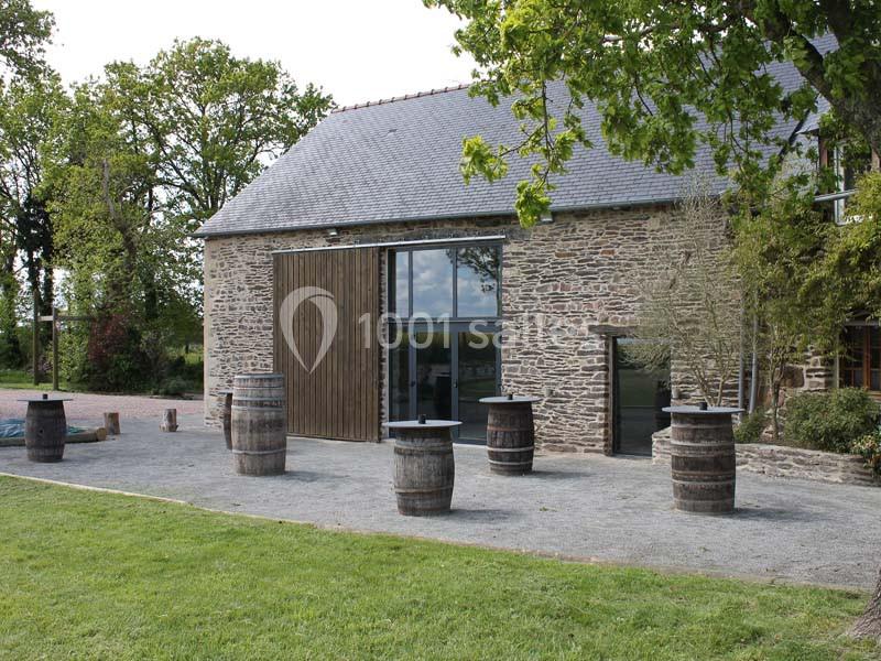 Bâtiment en pierre avec toit en ardoise, entouré de barriques en bois sur une cour gravillonnée et pelouse adjacente.