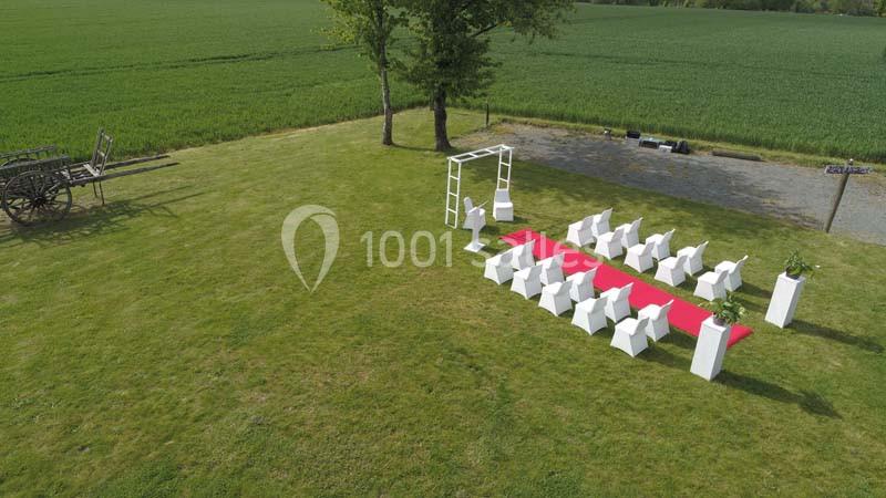 Disposition d'une cérémonie en plein air avec chaises blanches, arche décorative et tapis rouge sur une pelouse près d'un…
