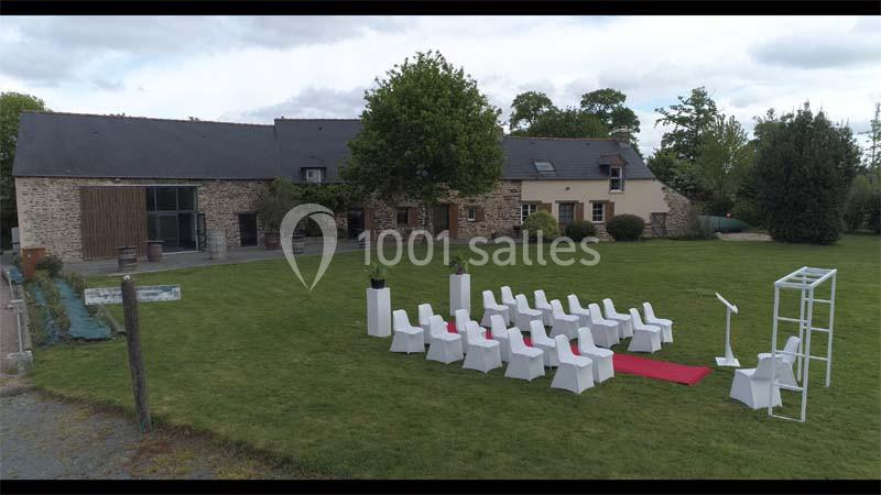 Disposition de chaises blanches sur une pelouse avec une arche et un tapis rouge devant un bâtiment en pierre.