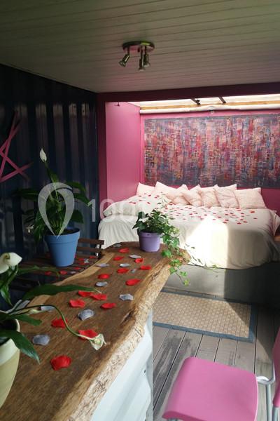 Intérieur d'une chambre colorée avec un lit décoré de pétales rouges, des plantes et une table en bois brut.