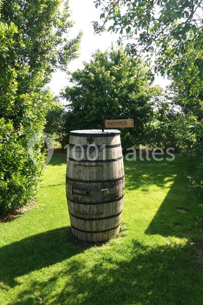 Tonneau en bois placé sur une pelouse verdoyante, entouré d'arbres, avec une pancarte indiquant ’Photomaton’.
