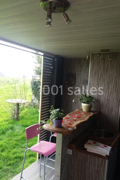 Vue d'un espace extérieur aménagé avec un comptoir en bois, des plantes en pot et des chaises roses près d'une pelouse.