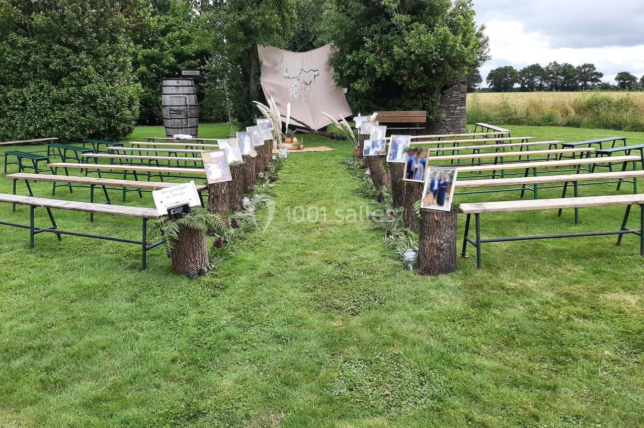Allée extérieure bordée de bancs en bois et décorée pour une cérémonie, avec un fond naturel et un décor champêtre.