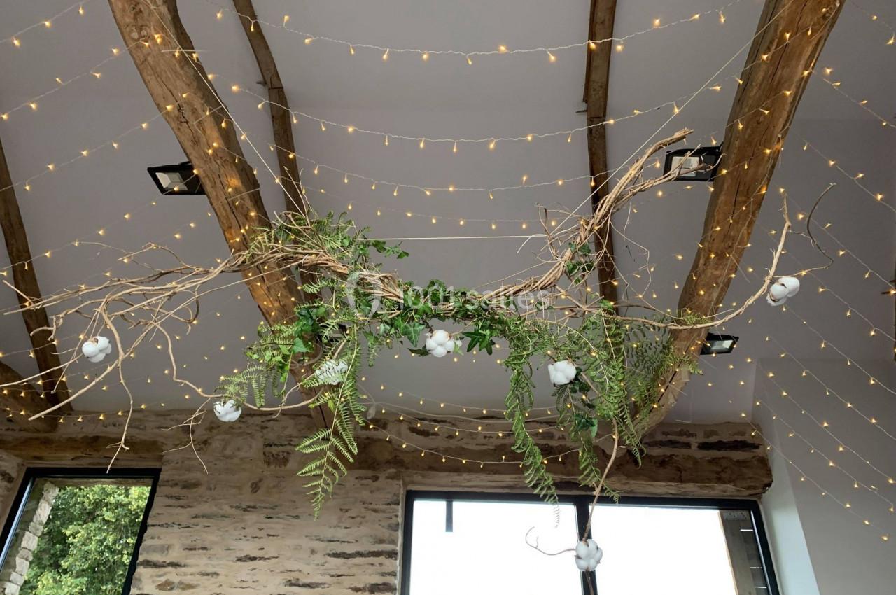 Guirlandes lumineuses suspendues à des poutres en bois avec des branches décoratives et feuillages verts.