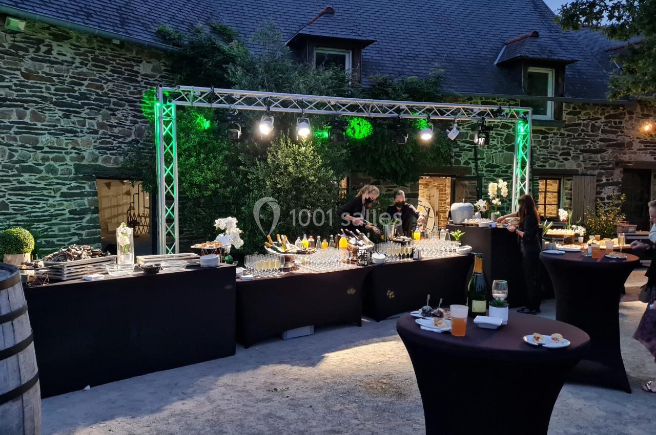 Buffet en extérieur avec tables hautes, éclairage nocturne et invités se servant dans un cadre en pierre.