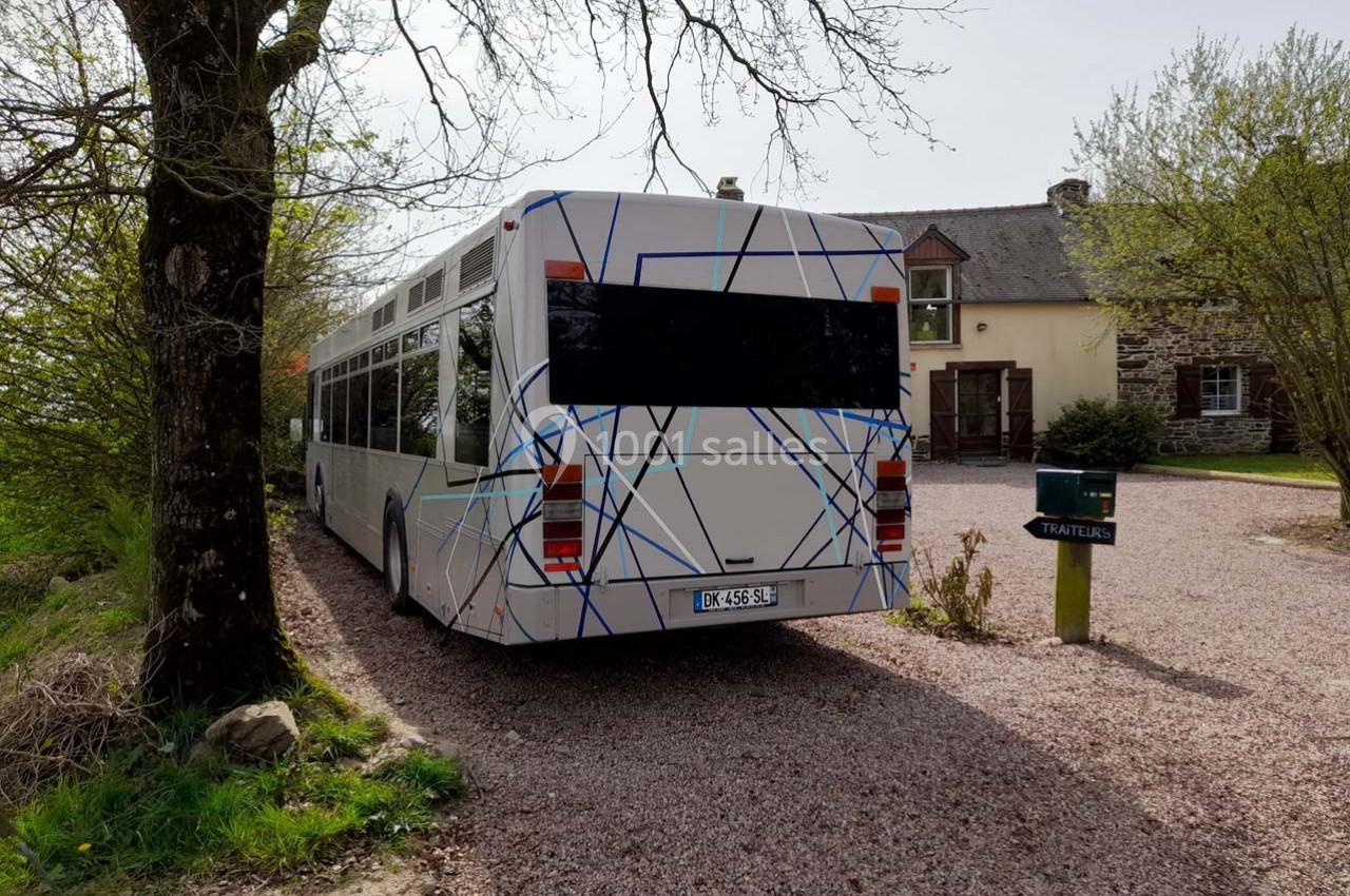 Autobus blanc stationné sur une allée gravillonnée devant une maison en pierre entourée de verdure.
