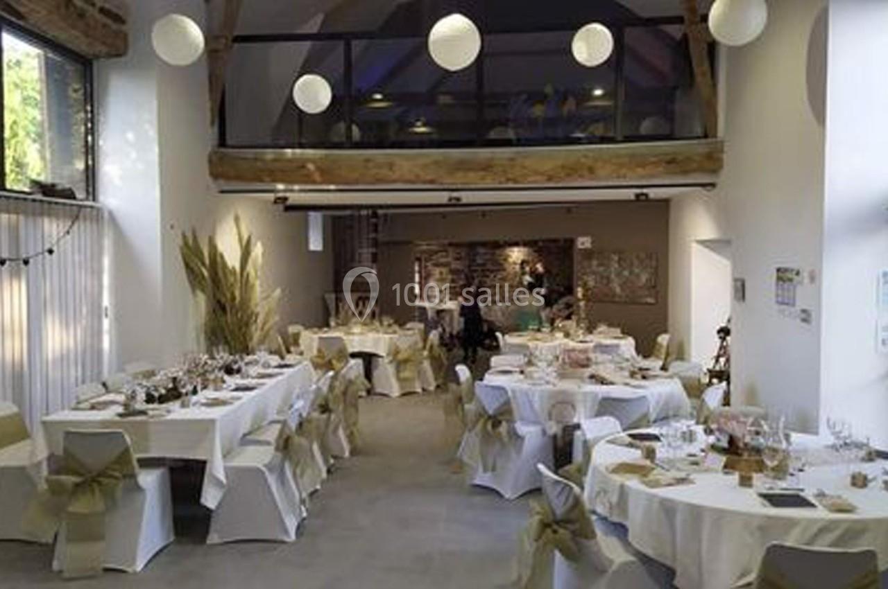 Salle de réception lumineuse avec tables décorées de nappes blanches et chaises ornées de rubans beiges.