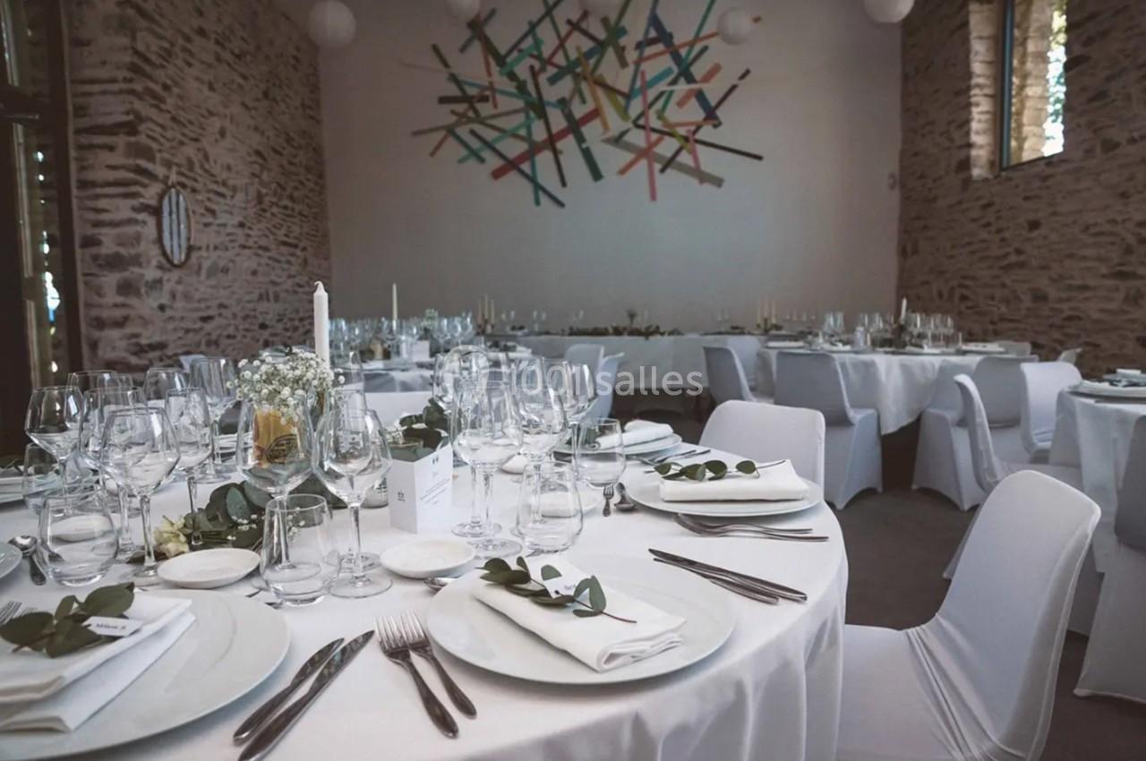 Salle de réception décorée avec des tables rondes dressées, nappes blanches et centre de table floral.