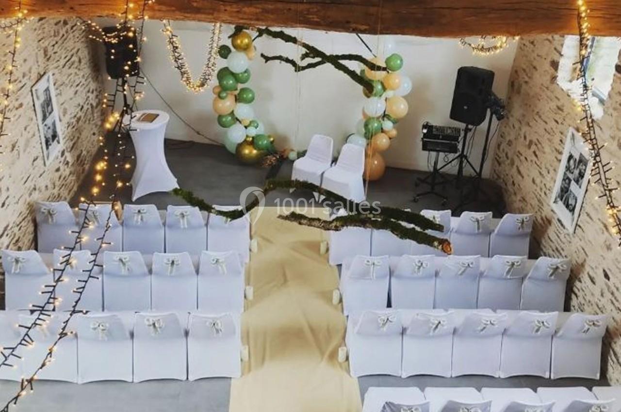 Salle décorée pour une cérémonie avec chaises blanches, arche ornée de ballons et guirlandes lumineuses suspendues.
