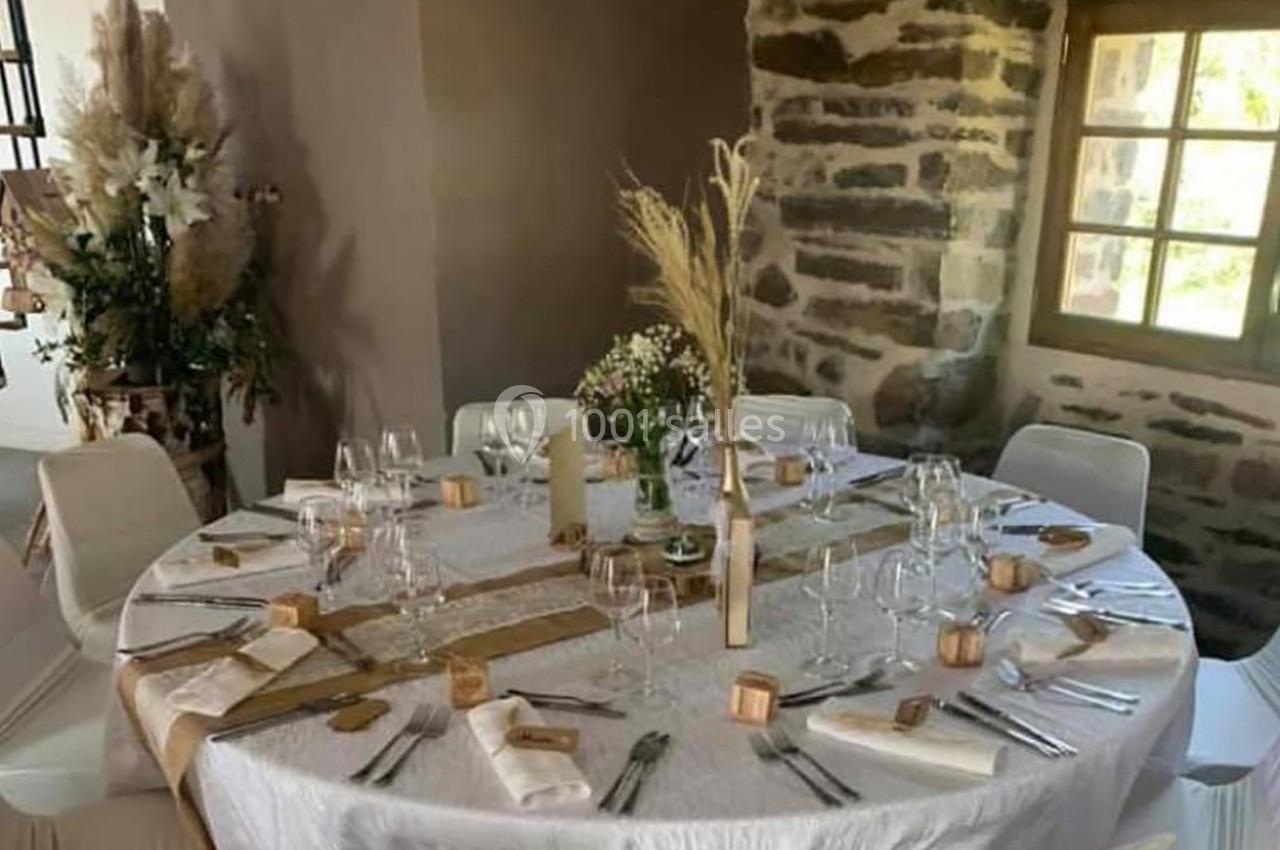 Table ronde décorée pour un repas, avec nappes blanches, couverts disposés, fleurs et éléments naturels en centre de table.