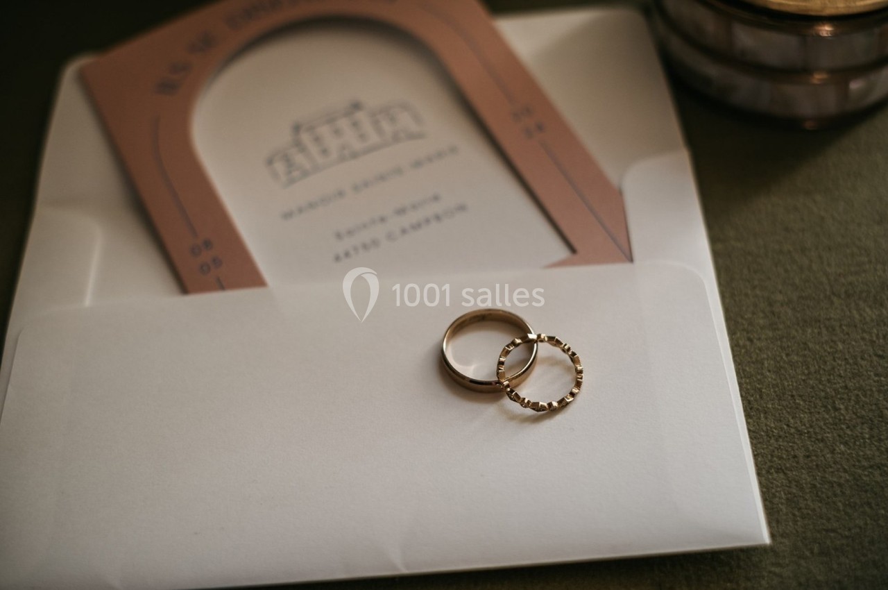 Deux alliances dorées posées sur une enveloppe blanche contenant une invitation de mariage.