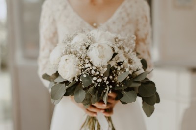 Robe de mariée en dentelle suspendue devant une fenêtre lumineuse avec vue sur un jardin verdoyant.